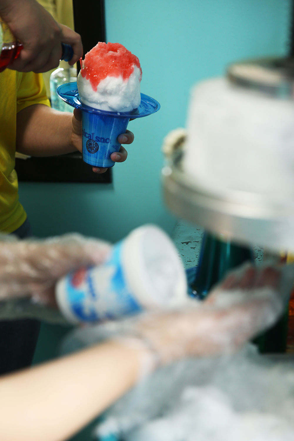 Riley Tomich adds the flavor syrup to a snow cone while coworker Cassie Downare catches the snow
